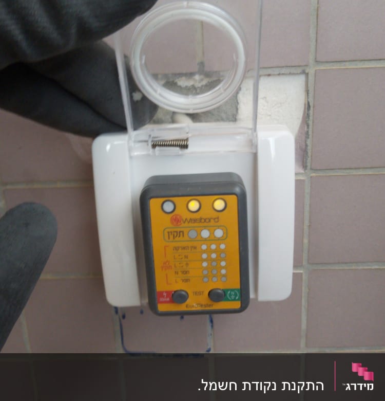 בודק חשמל עם כיסוי שקוף על קיר אריחים